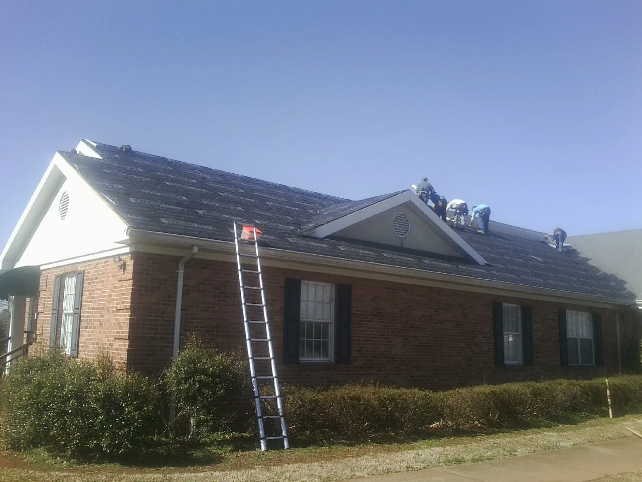 Crew tearing shingles off a brick ranch roof with a ladder set — Metal Roof Repair work by our crew in Cockeysville