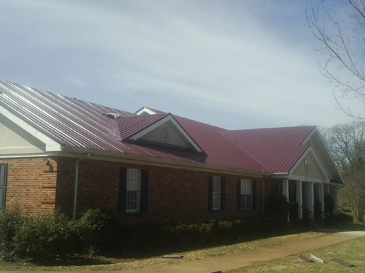 Red metal roof with gabled entries on a long brick building, from a Hail Damage Roof Repair job in Cockeysville