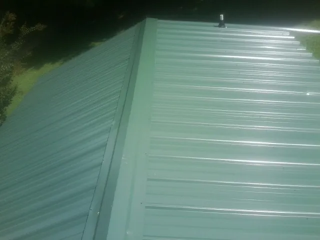New green metal panels meeting at the ridge of a roof — Flat Roof Repair work by our crew in Cockeysville