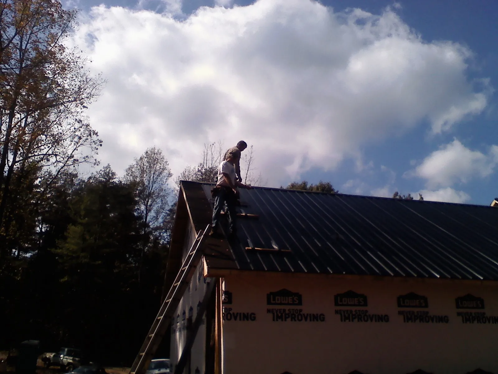 Roofer fastening dark metal panels high against a cloudy sky, from a Roof Inspection job in Cockeysville