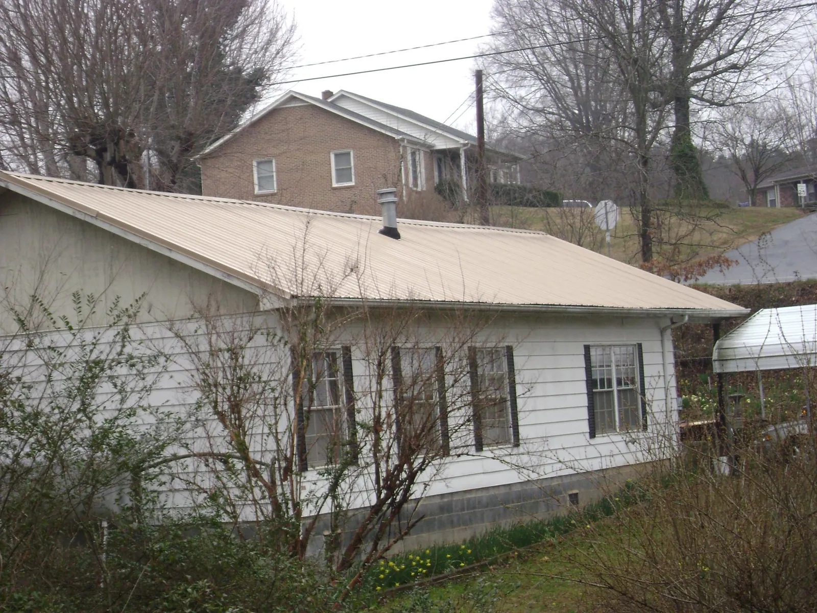 Tan metal roof on a white sided house set into a hillside — Commercial Roofing by Roofing Brothers in Cockeysville